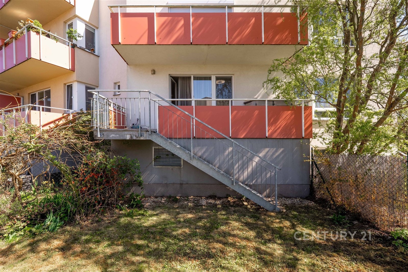 Balkon s kovovým zábradlím, vstupem do bytu, orientován na jih, obklopený zelení, ideální pro relaxaci nebo letní stolování.