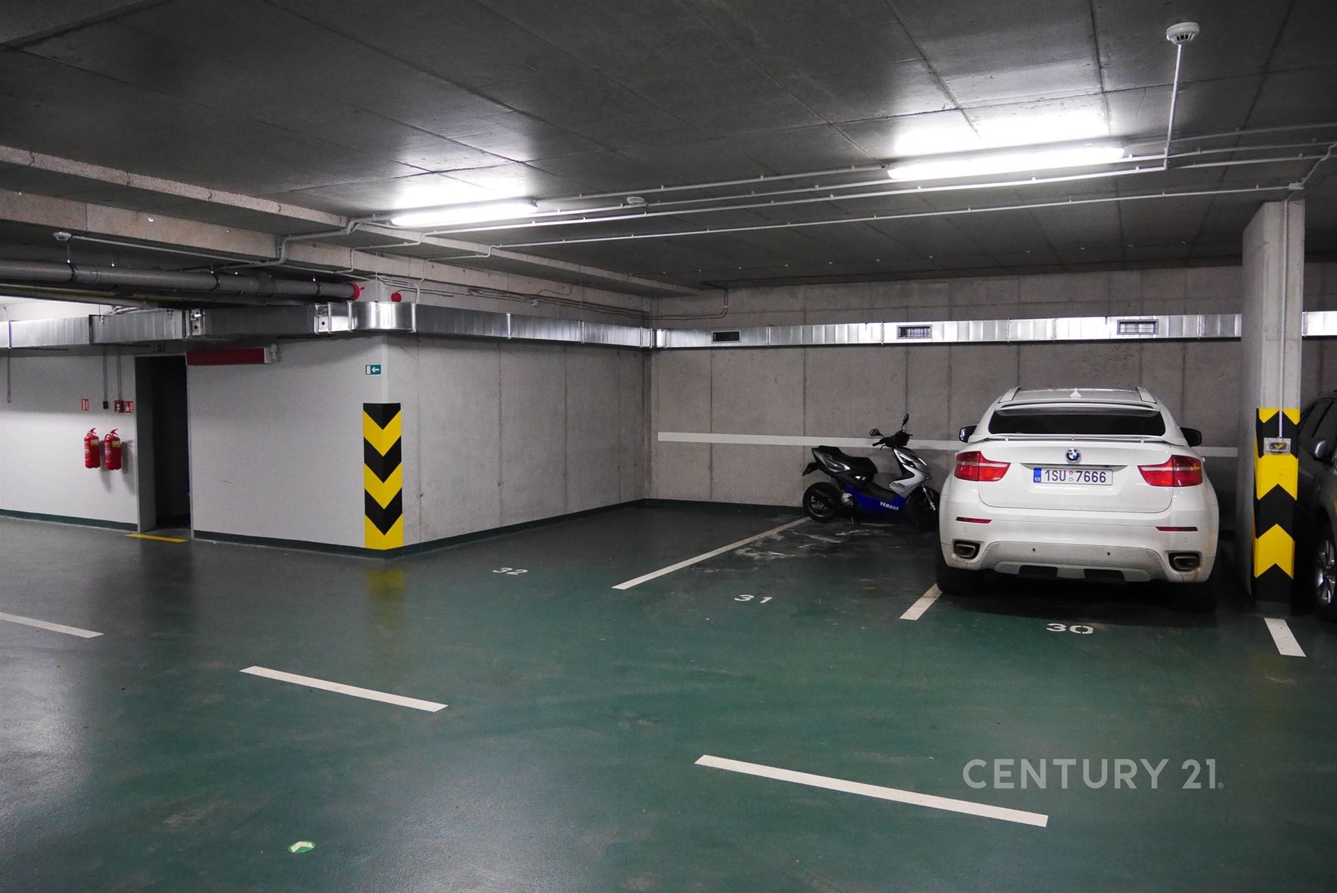 Podzemní parkovací garáž s moderním osvětlením, betonovými stěnami a parkovacími místy, vhodná pro bezpečné a kryté parkování.