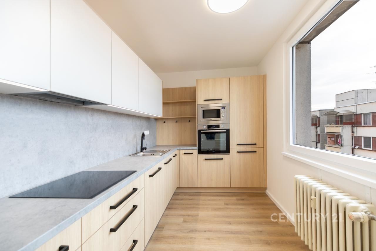 Moderní kuchyň s parketovou podlahou, vestavěnými spotřebiči a velkým oknem. Světlý a elegantní design nabízí praktické úložné prostory.