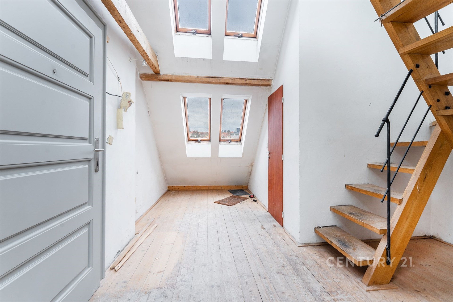 Podkrovní prostor s dřevěnou podlahou, světlý díky střešním oknům, dřevěné schodiště do patra, moderní a vzdušný design.