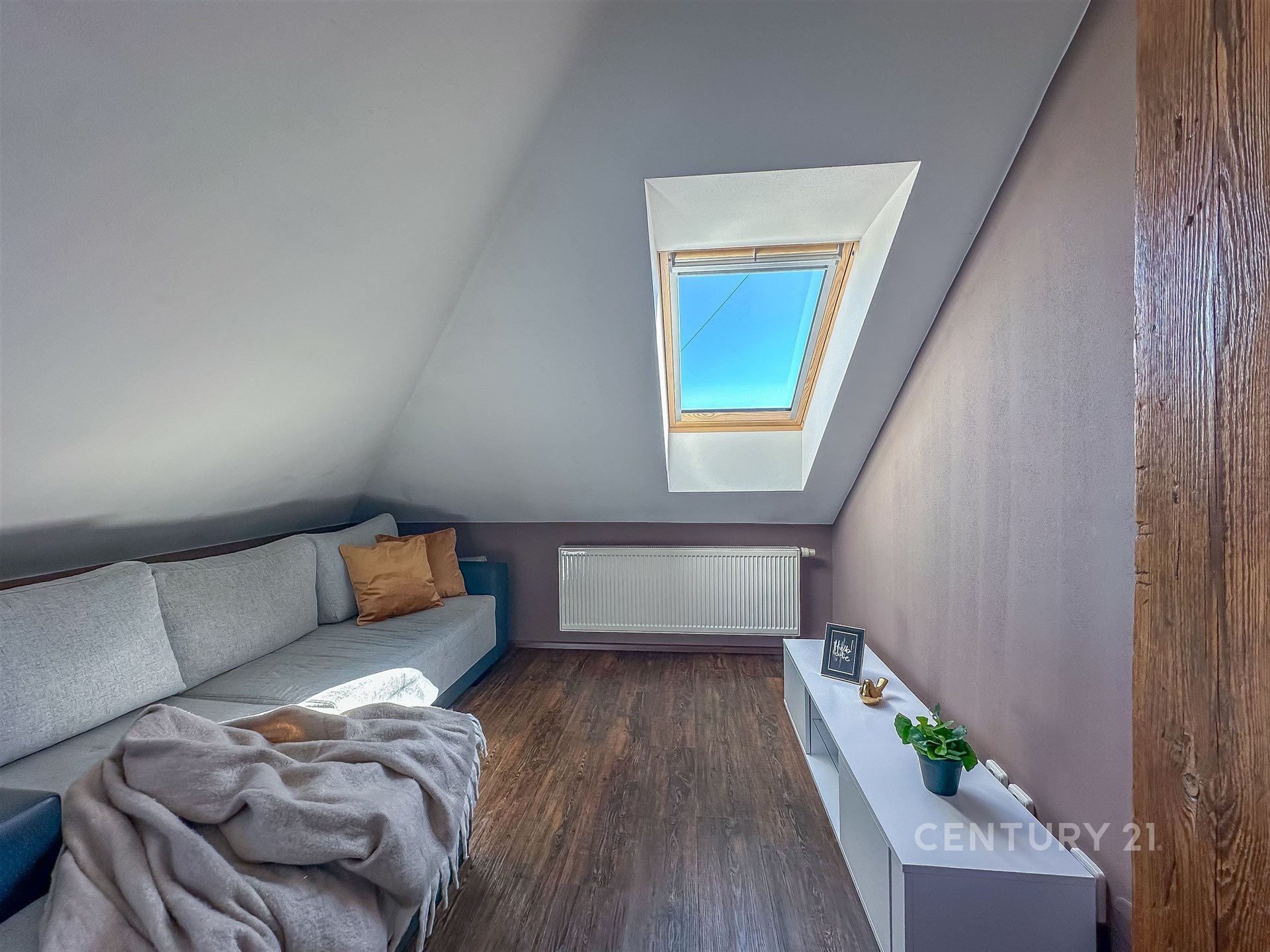 Podkrovní obývací pokoj s dřevěnou podlahou, velkým střešním oknem a moderním nábytkem vytváří světlý a útulný prostor.