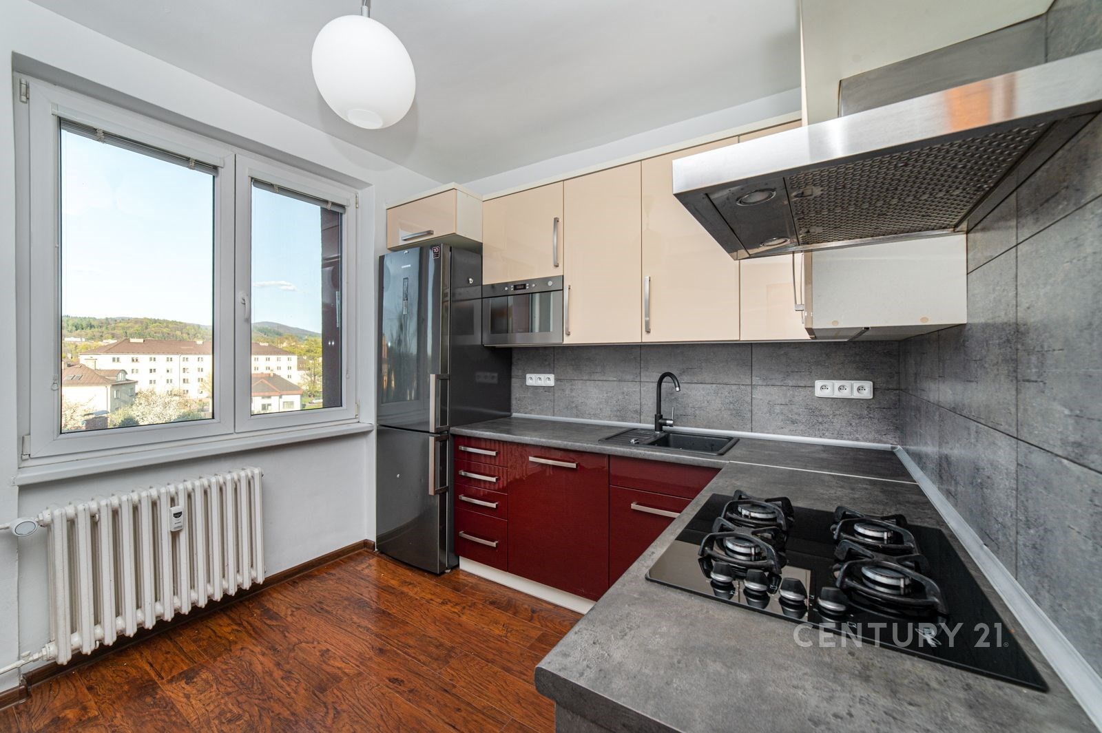 Moderní kuchyň s dřevěnou podlahou nabízí vestavěné spotřebiče, tmavou pracovní desku a velká okna pro dostatek světla.