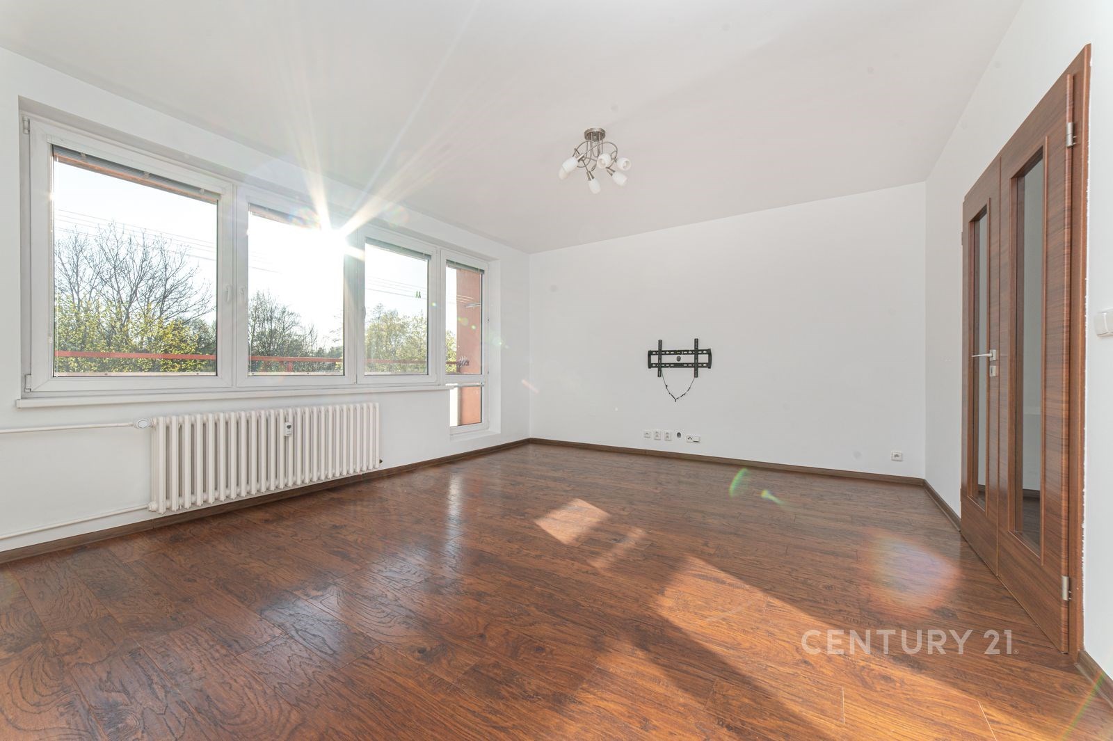 Světlý obývací pokoj s parketovou podlahou, velká okna a moderní dveře vytvářejí prostorný a vzdušný interiér.