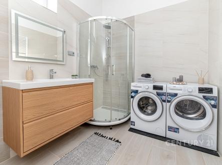 Koupelna s moderní sprchou, dřevěnou skříňkou, světlé dlaždice a pračkou se sušičkou, prostorná a světlá.