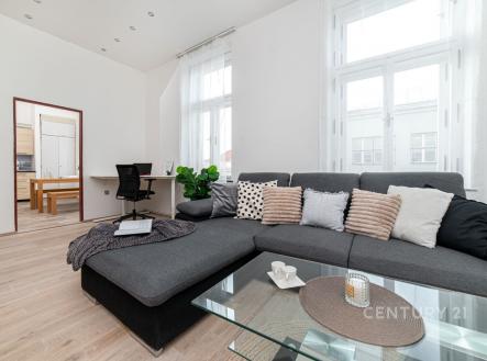 Světlý obývací pokoj s parketovou podlahou a velkými okny, moderní sedací souprava a stylový skleněný konferenční stolek