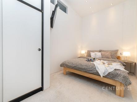 Světlá ložnice s moderním designem, vestavěné skříně, světlý koberec a minimalistické osvětlení vytváří útulnou atmosféru.