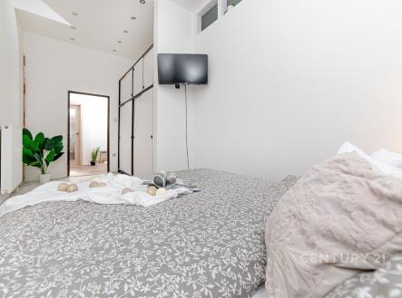 Světlá ložnice s moderním designem, vestavěné skříně, parketová podlaha a prostorný interiér s minimalistickými dekoracemi.