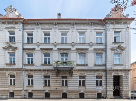 Historická budova s dekorativní fasádou a balkonem, zdobené detaily a udržovaný vchod, ideální pro městské bydlení.