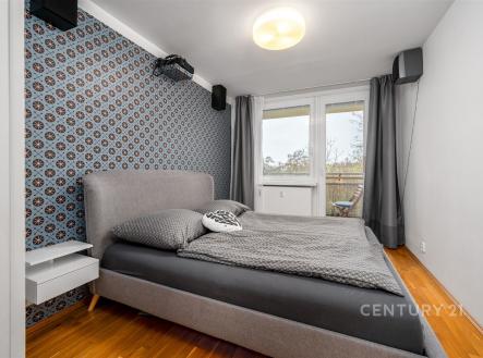 Stylová ložnice s dřevěnou podlahou, velkými okny a moderní tapetou. Světlý a útulný prostor ideální pro relaxaci.