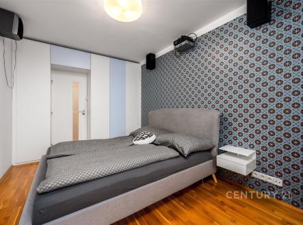 Prostorná ložnice s parketovou podlahou, vestavěnými skříněmi a moderními tapetami na stěně, nabízí elegantní a útulný prostor k odpočinku.