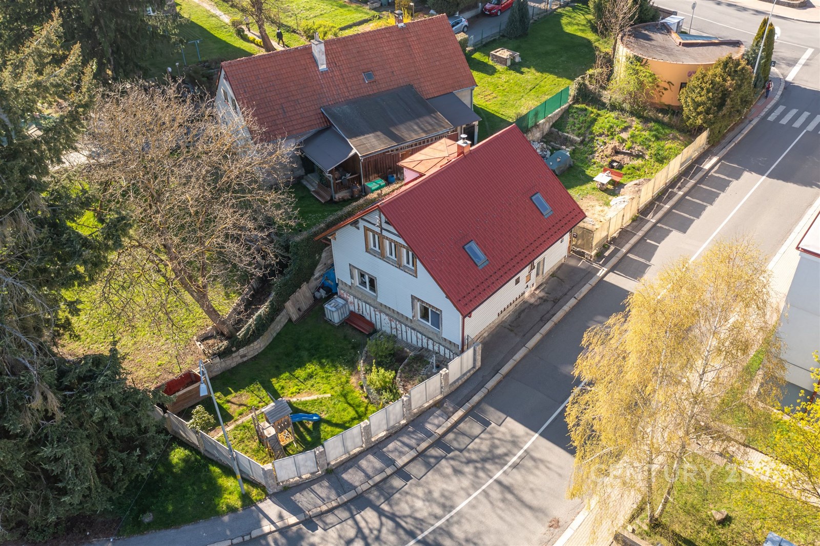 Rodinný dům s červenou střechou, obklopený zahradou, oplocený plotem. Klidná lokalita v blízkosti přírody, ideální pro rodinné bydlení.
