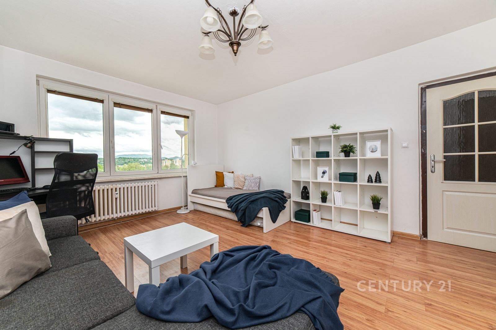 Světlý obývací pokoj se světlou parketovou podlahou, velkými okny a moderními vestavěnými regály, vytváří příjemnou atmosféru pro bydlení.