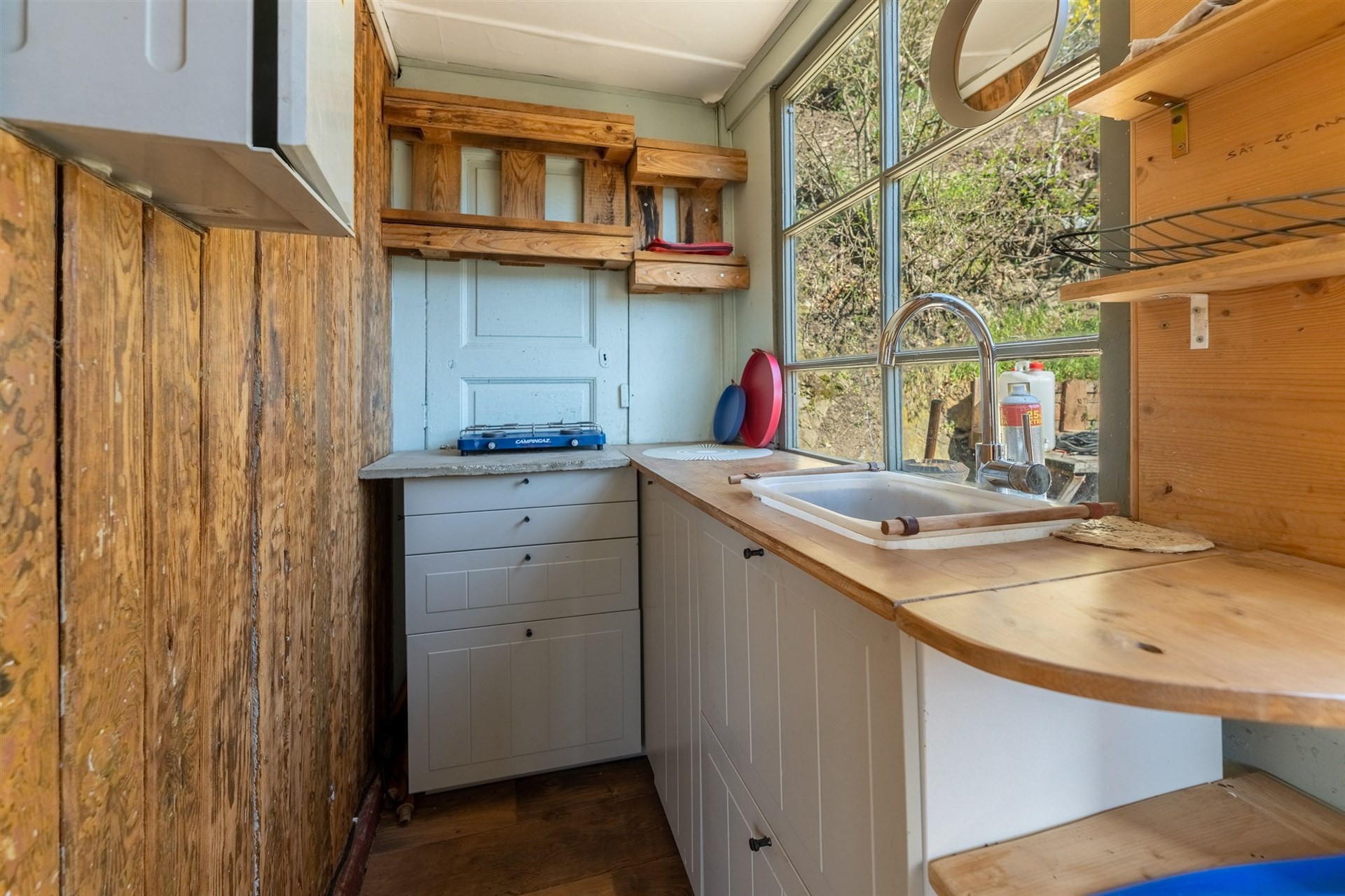 Kompaktní kuchyň s dřevěnými prvky, světlou linkou a velkými okny. Stylová dlažba a rustikální design dodávají útulný pocit.