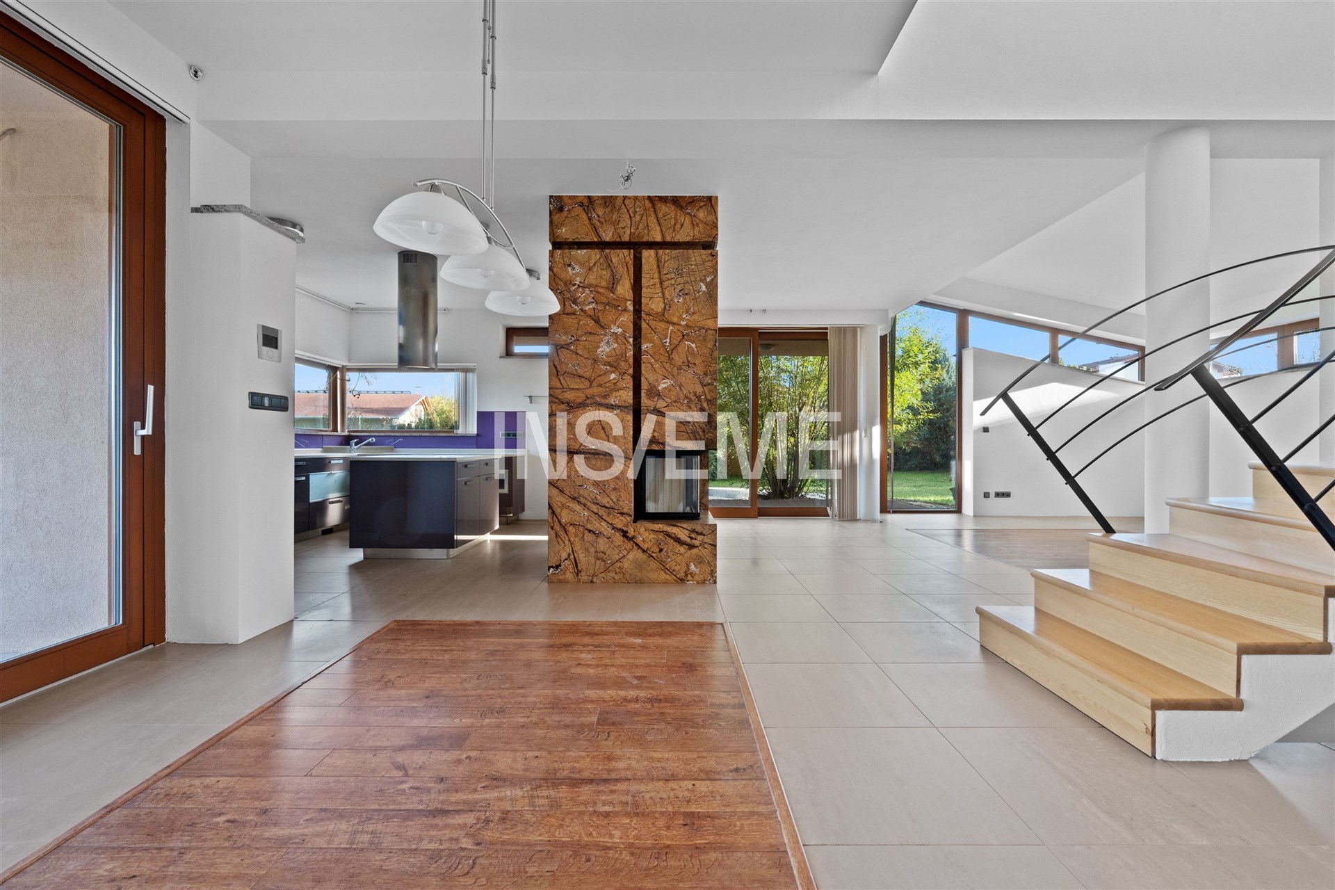 Prostorný obývací pokoj s parketovou podlahou a krbovými kamny, velká okna zajišťují světlý interiér, moderní architektonické prvky.