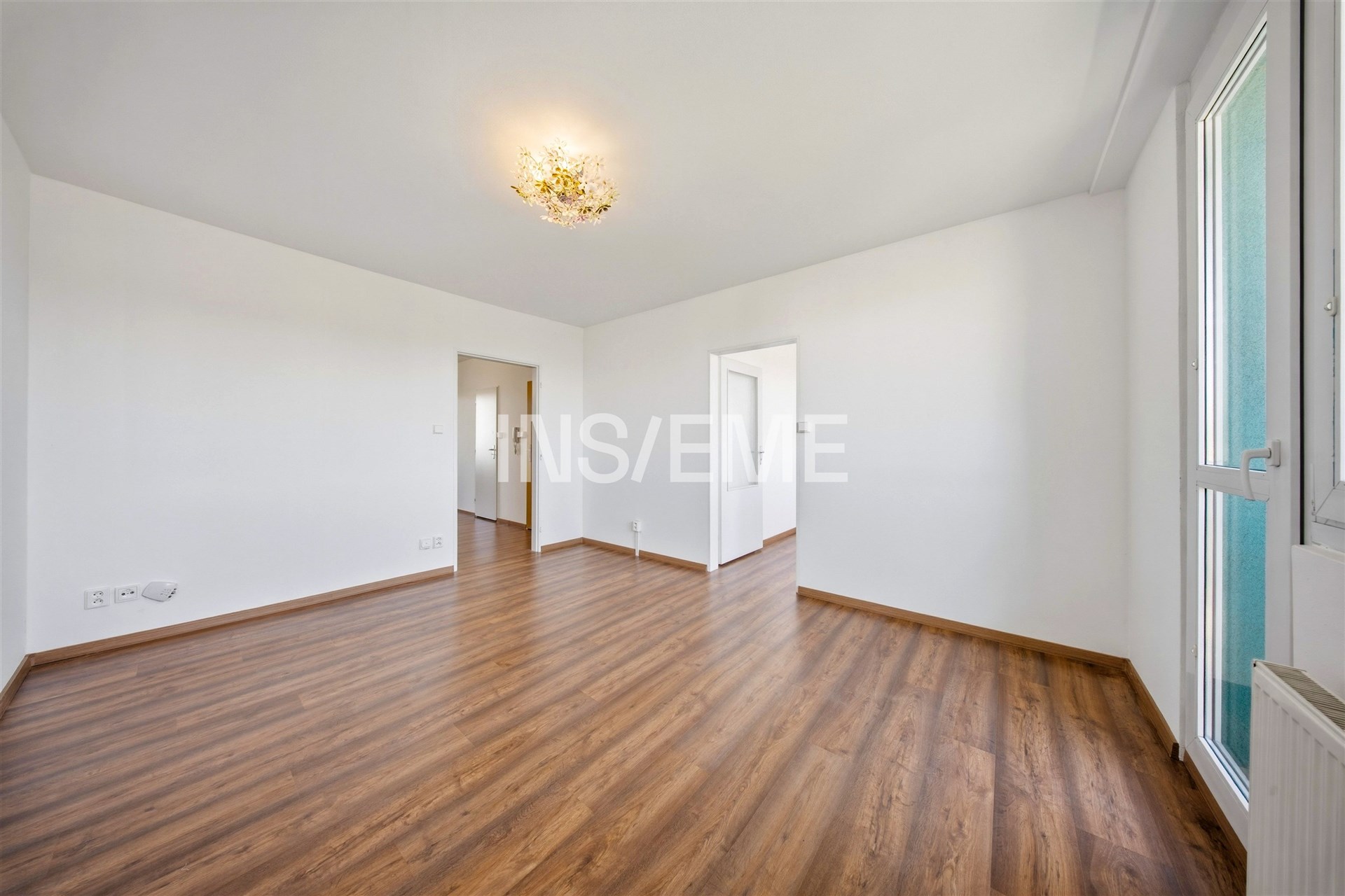 Světlý obývací pokoj s parketovou podlahou, velkými okny a moderním osvětlením. Prostor nabízí moderní design a příjemnou atmosféru.