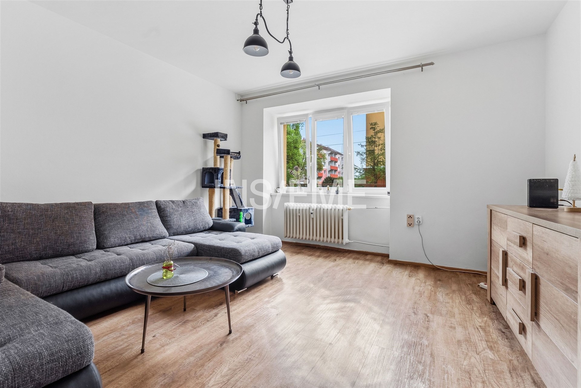 Moderní obývací pokoj s parketovou podlahou, velkým oknem a rohovou sedačkou, světlý interiér dodává prostoru vzdušnost a útulnost.