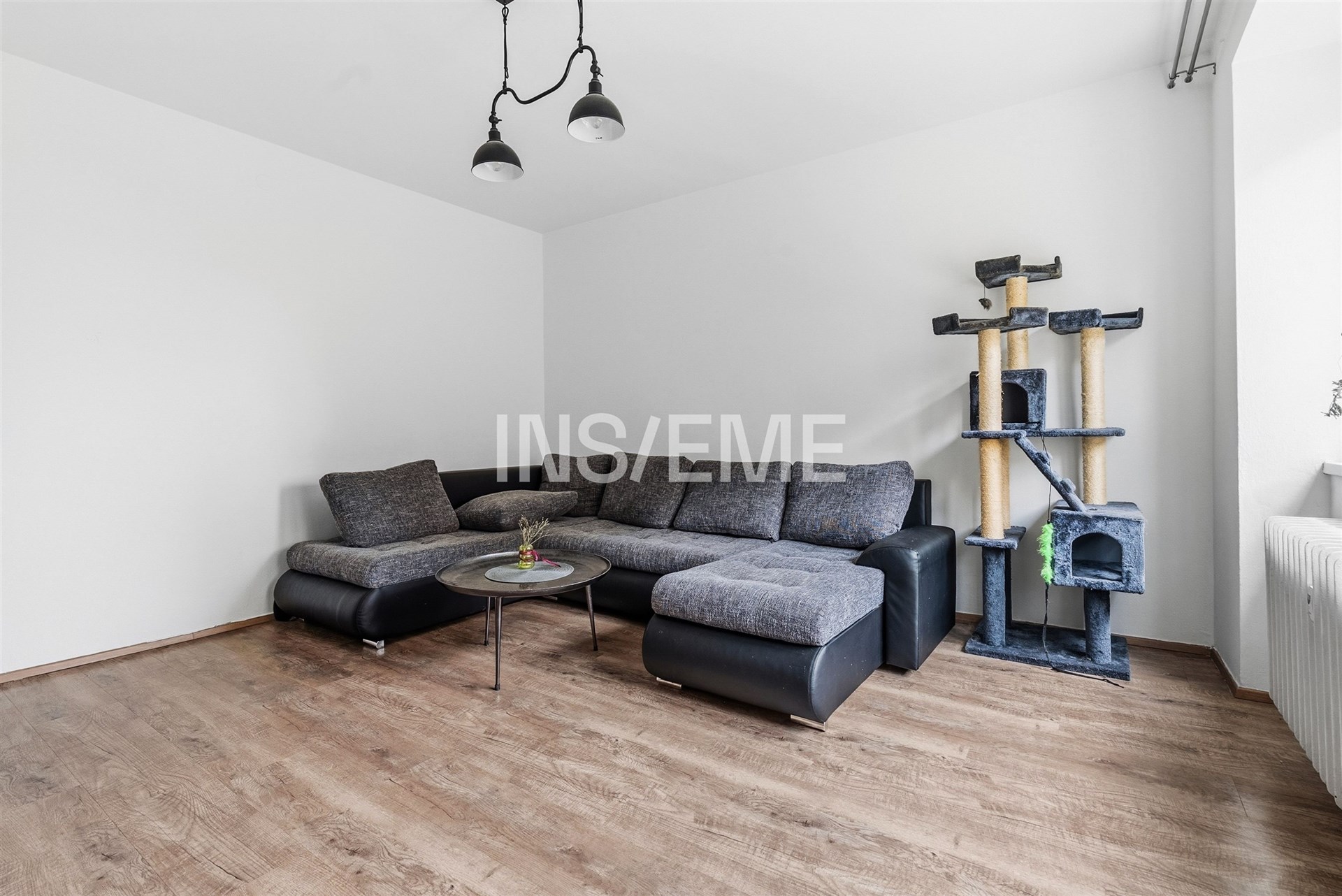 Světlý obývací pokoj s parketovou podlahou, prostornou sedací soupravou a moderním osvětlením. Velká okna zajišťují dostatek přirozeného světla.