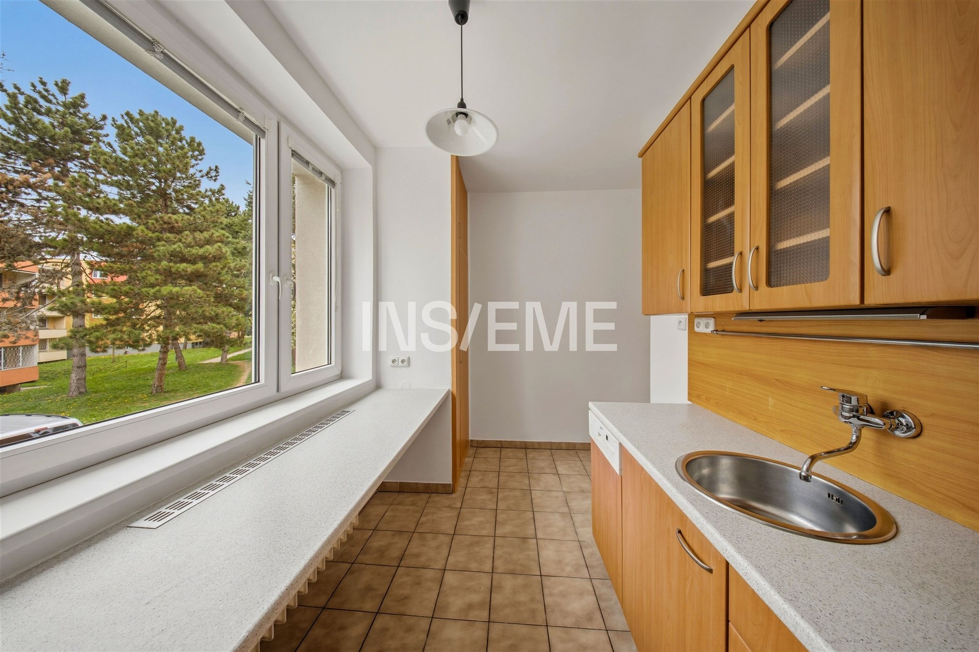 Kuchyň s velkými okny, dlažbou a vestavěnými skříněmi, moderní design a světlé prostředí.