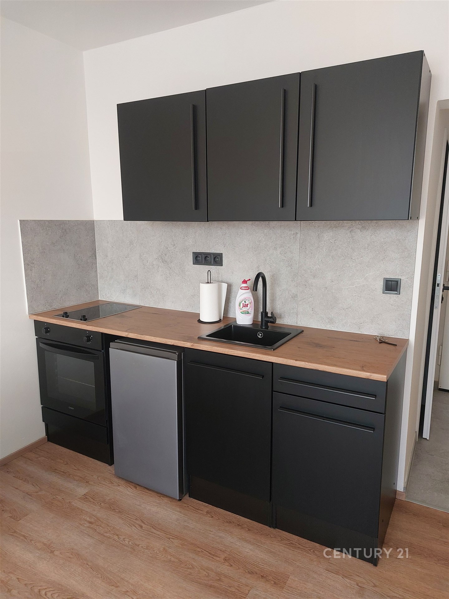 Moderní kuchyň s dřevěnou pracovní deskou, černými skříňkami a parketovou podlahou vytváří elegantní a funkční prostor.