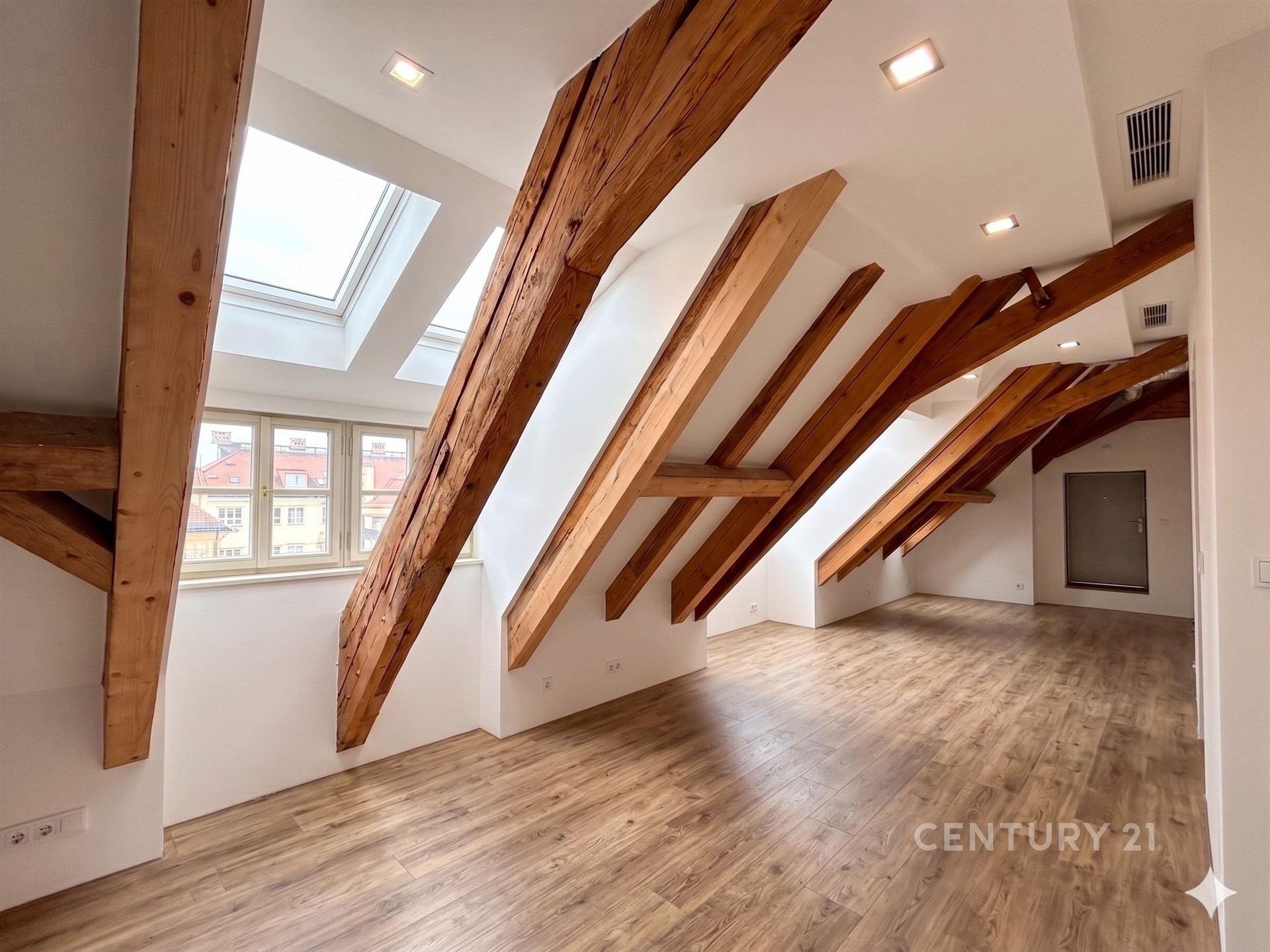 Podkrovní prostor s dřevěnými trámy, světlou parketovou podlahou a velkými okny, moderní design a prostorný interiér.
