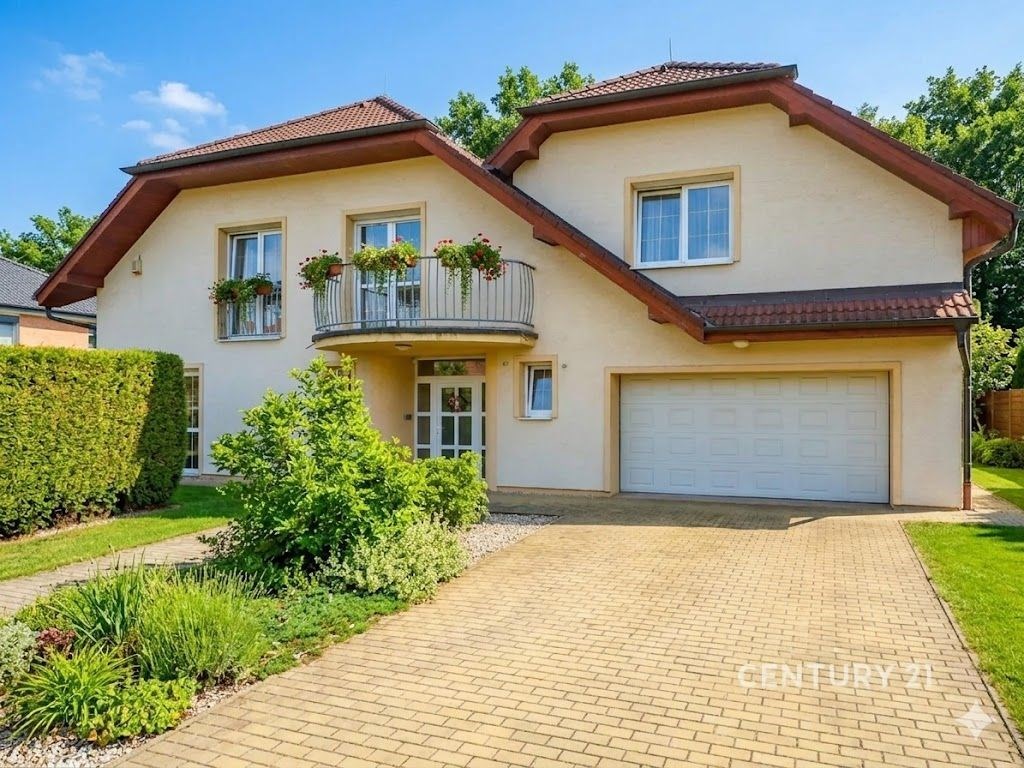 Dvoupodlažní rodinný dům s upravenou zahradou, velkou garáží a balkonem. Fasáda ve světlých barvách, moderní architektura, klidná rezidenční lokalita.