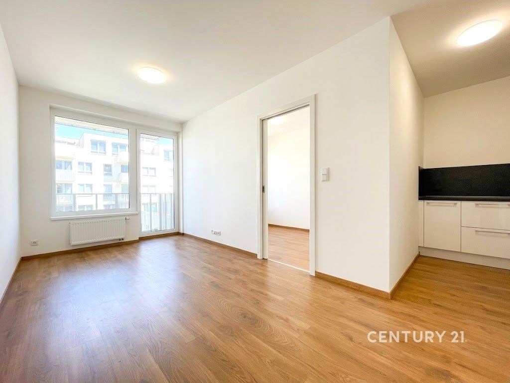 Světlý obývací pokoj, parketová podlaha, moderní design, velká okna, přístup na balkon, propojený s kuchyňským koutem.