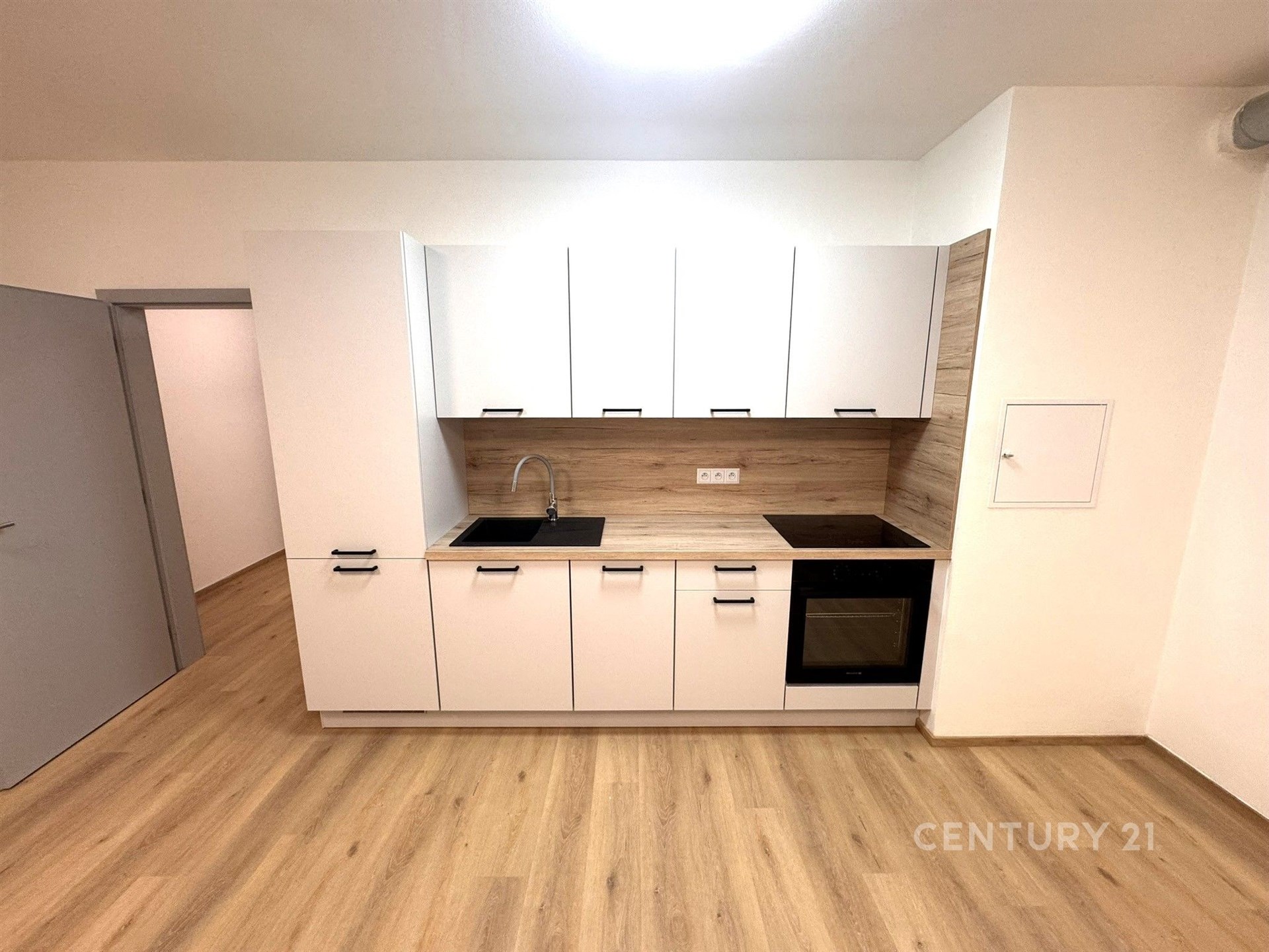 Moderní kuchyň s parketovou podlahou, světlými bílými skříňkami a dřevěným obkladem, vestavěné spotřebiče, minimalistický design.