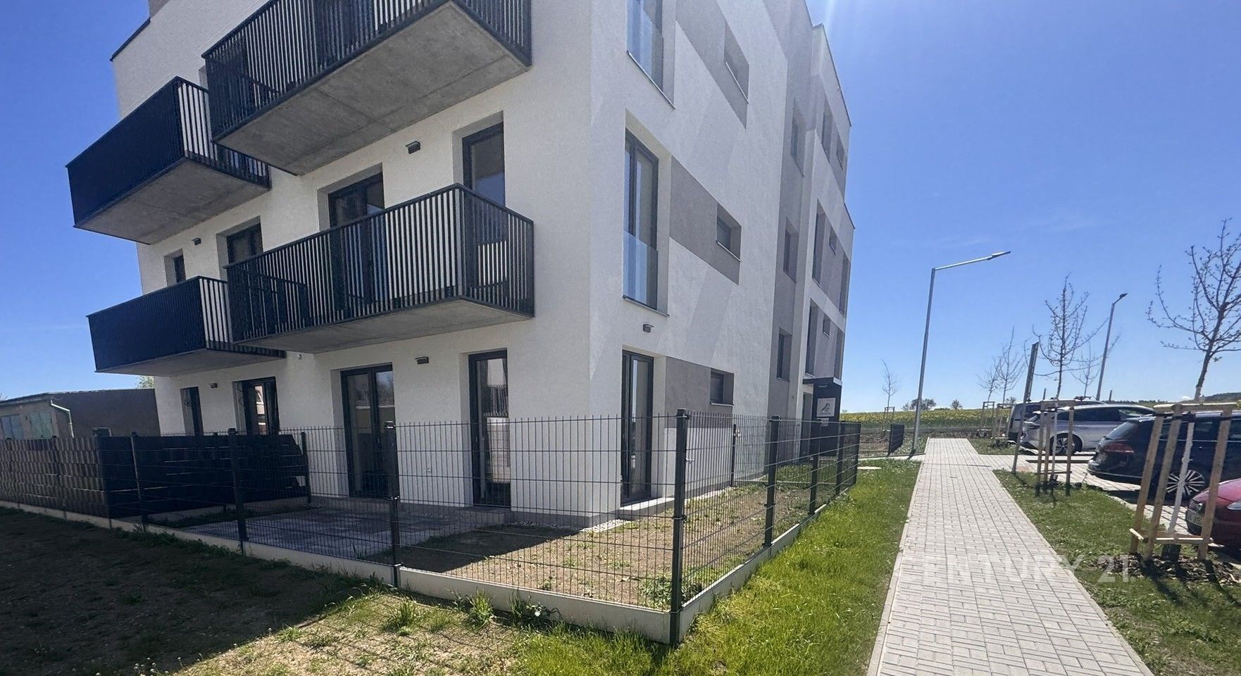 Moderní bytový dům s balkony, bílou fasádou a udržovaným trávníkem, v klidné lokalitě.