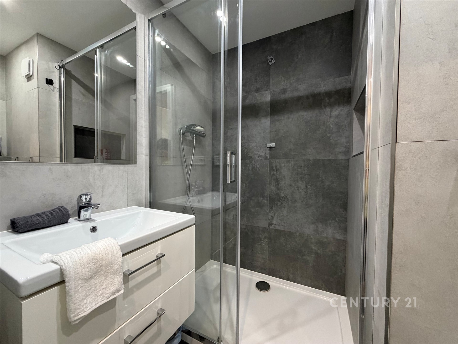 Moderní koupelna s proskleným sprchovým koutem, dlažbou a vestavěným umyvadlem. Světlý interiér s elegantním designem.