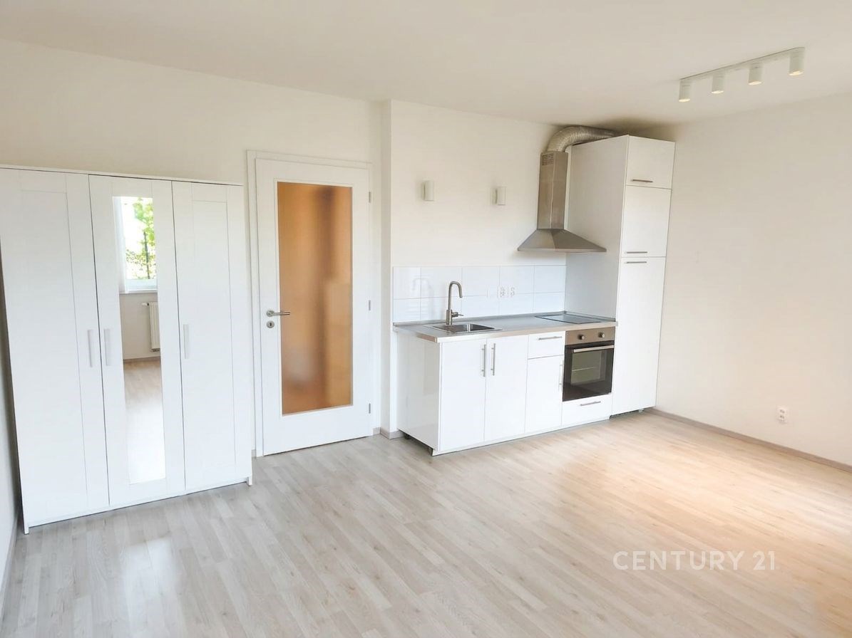 Světlá moderní kuchyň s vestavěnými spotřebiči, parketová podlaha, světlý dekor, minimalistický styl, bílé skříňky a nerezová digestoř.