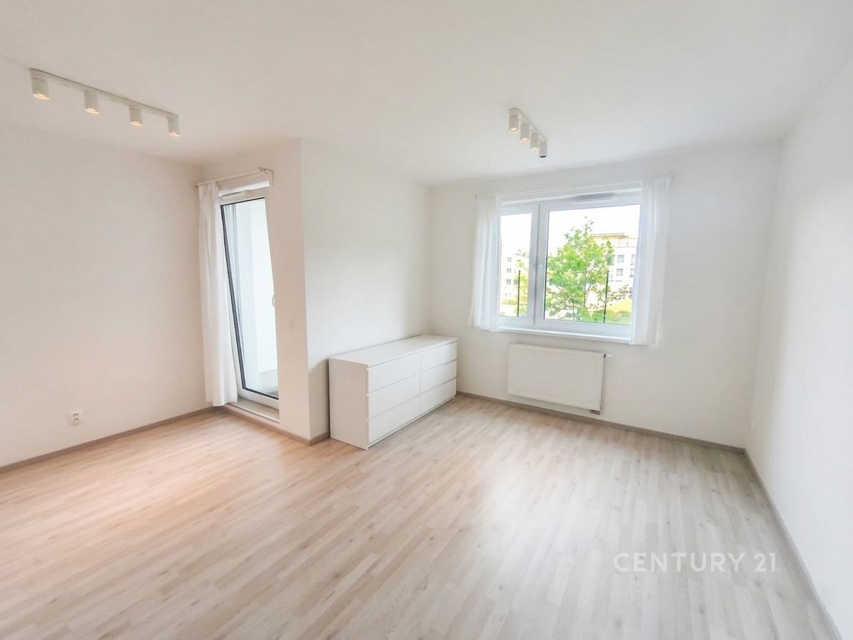 Světlý obývací pokoj s parketovou podlahou, velkými okny a moderním osvětlením nabízí pohodlný a svěží prostor k relaxaci.