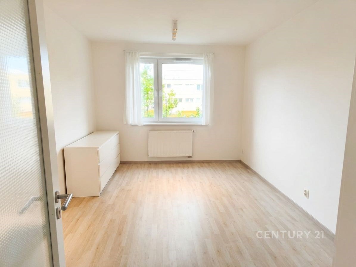 Světlá ložnice s parketovou podlahou, velká okna nabízejí dostatek přirozeného světla, moderní povrchy zdůrazňují čistý design.