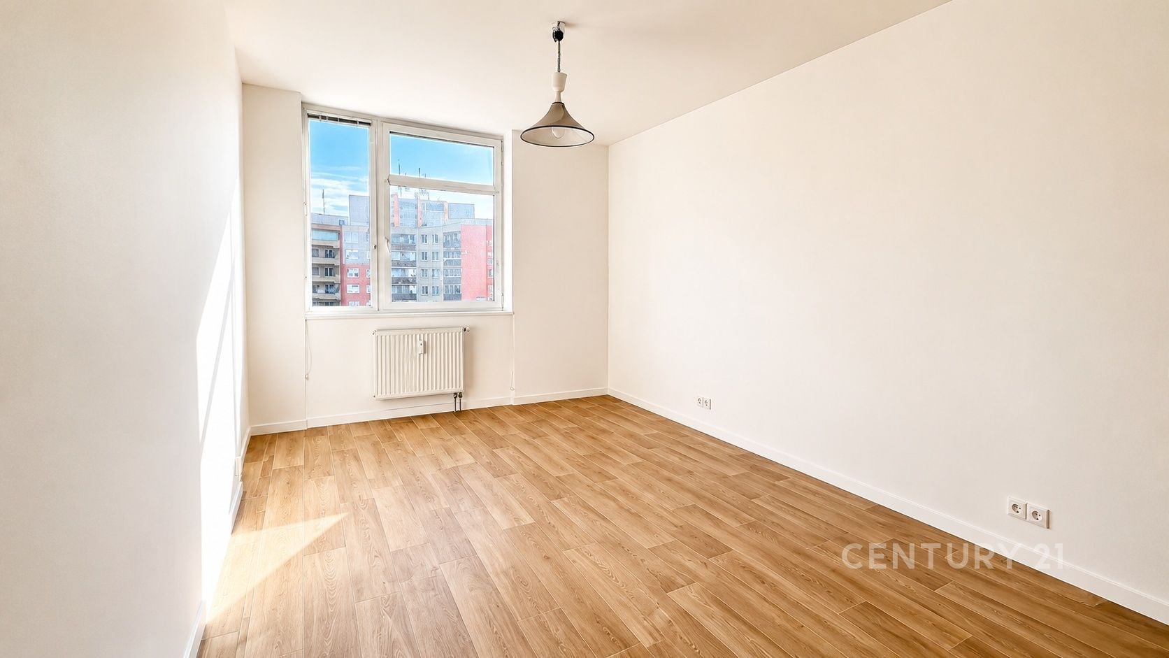 Světlý pokoj s dřevěnou podlahou, velkými okny a moderní výmalbou.